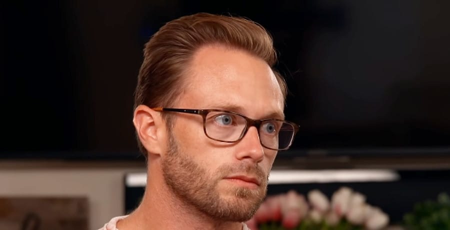 A man in black glasses and short hair looking glum