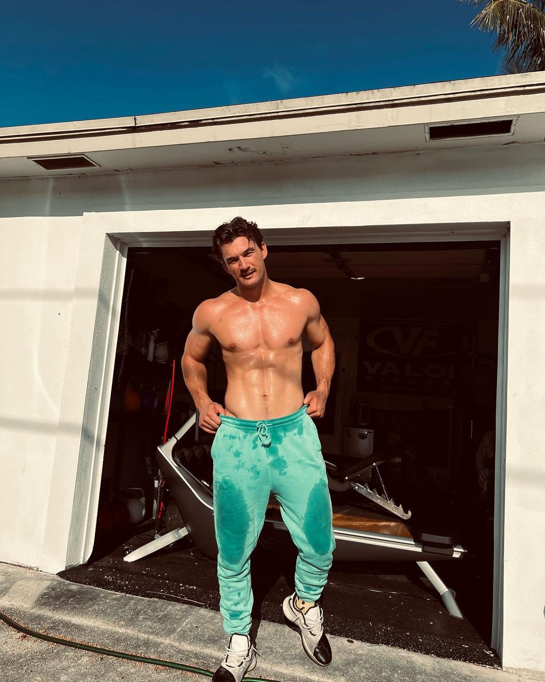 Tyler Cameron - a man in green sweatpants without a shirt on, showing off his muscles