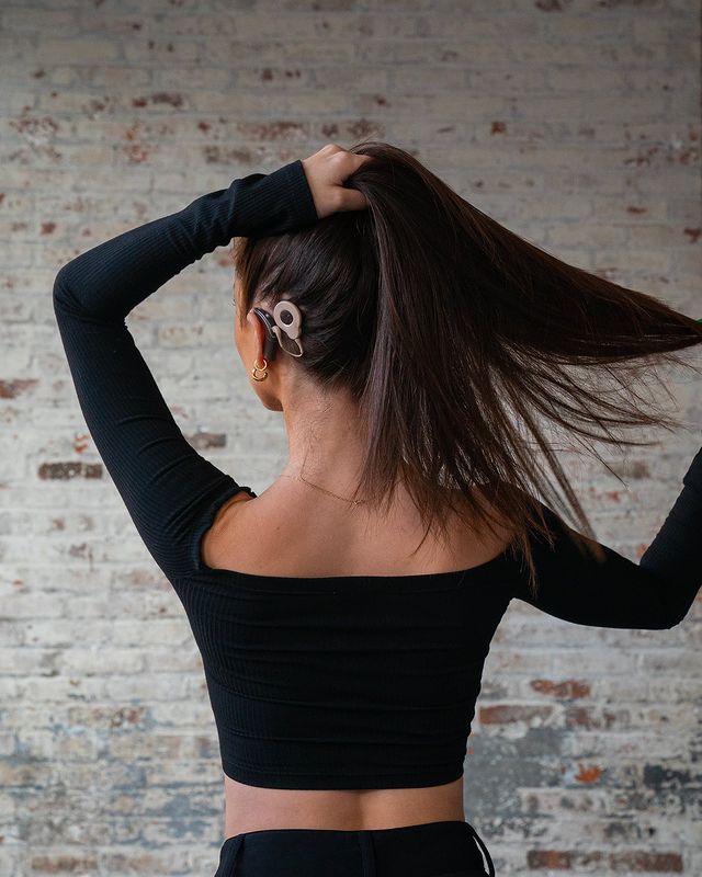 The back of a woman holding her hair in a ponytail to show her cochlear implant