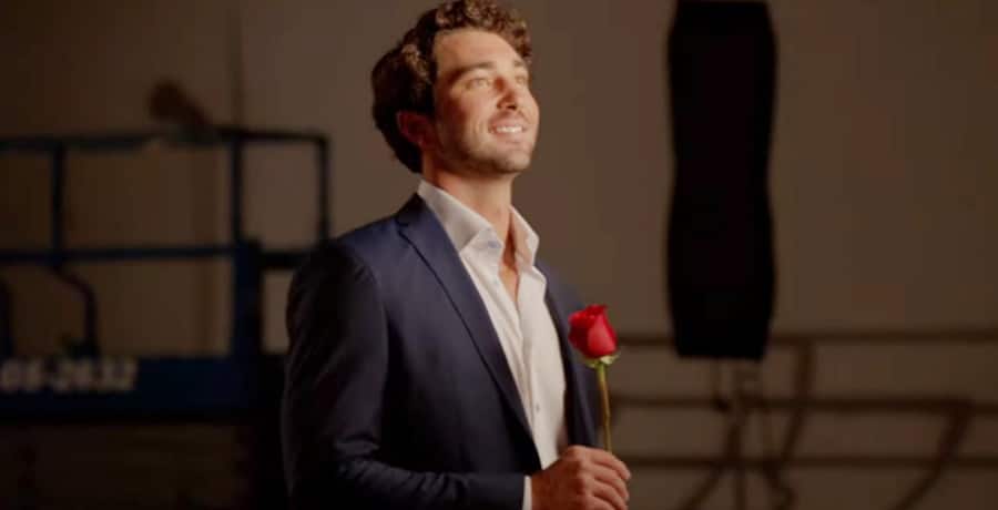 A man with brown hair in a blue tuxedo holding a red rose.