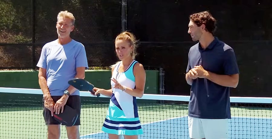 Two men and a woman standing in front of a tennis net.