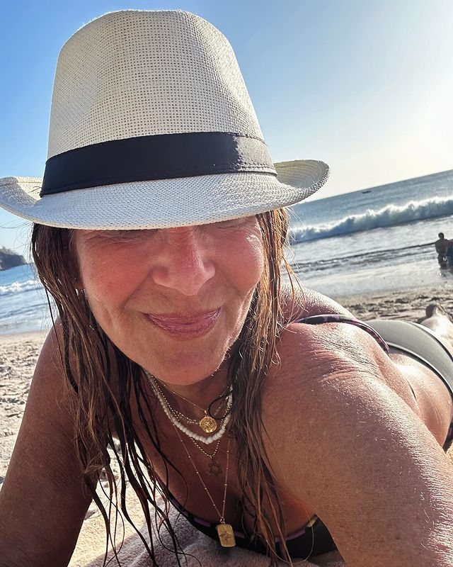 A woman on the beach wearing a black bikini and a white hat that covers her face.
