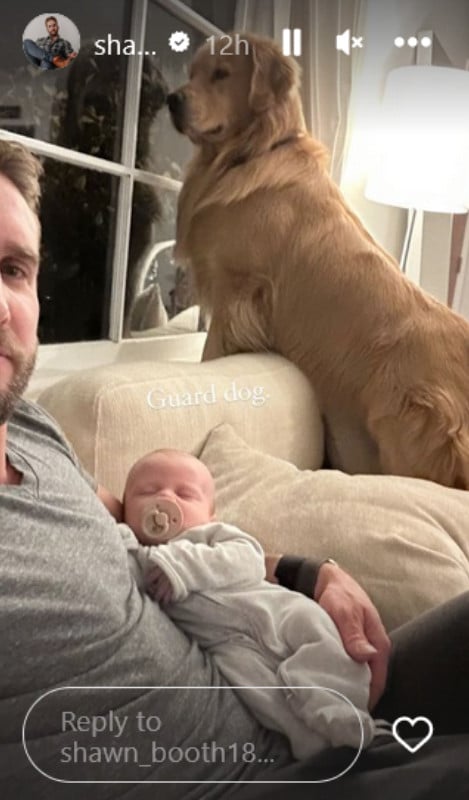 A man holding a baby with a yellow dog next to them on a couch.