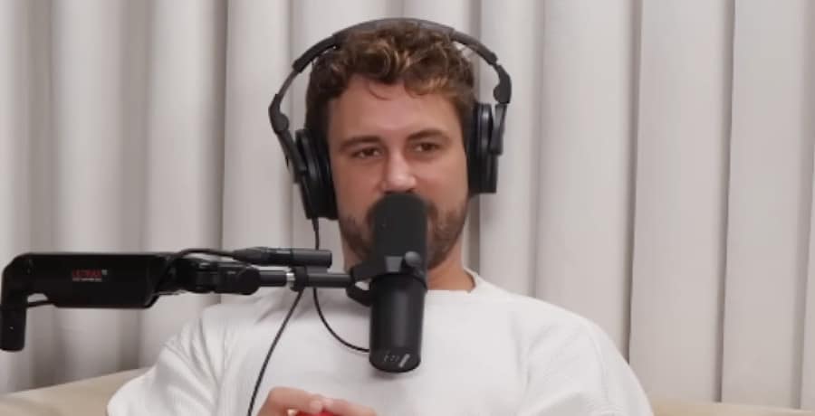 A man with short, curly brown hair wearing earphones and talking into a microphone.