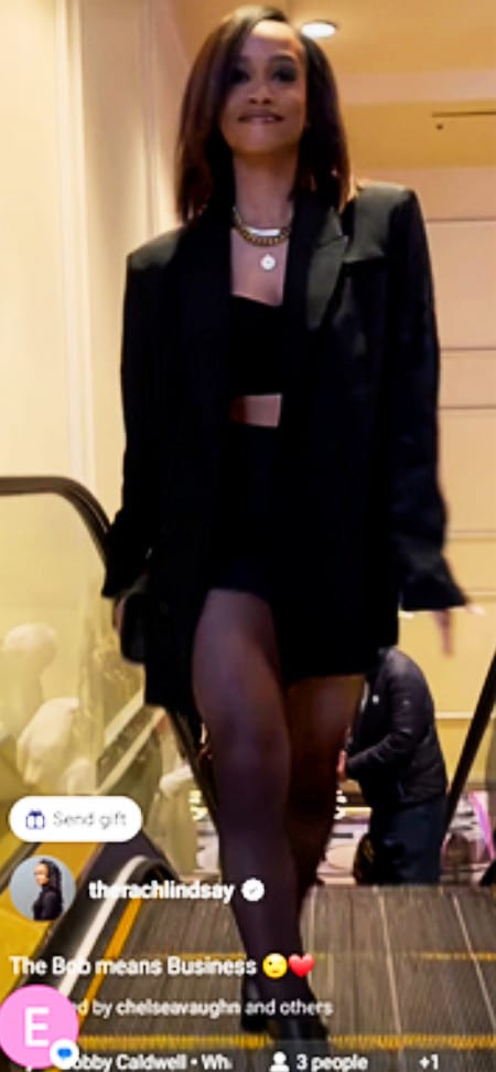 A black woman wearing a long black jacket over black shorts and a black crop top.