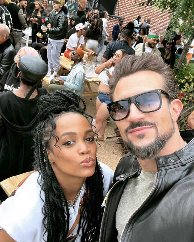 A black woman with her hair piled on top of her head standing next to a white man wearing sunglasses.