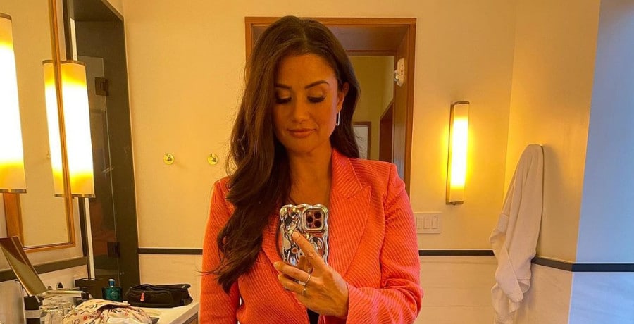 A woman with long brown hair in an orange jacket.