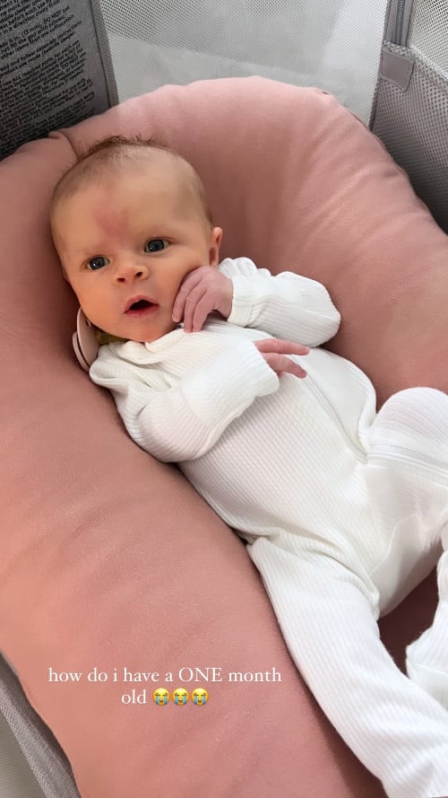A one-month-old baby in a white onesie.