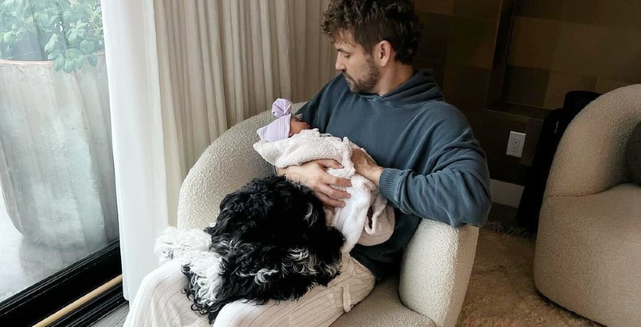 A man holding a baby with dog on lap