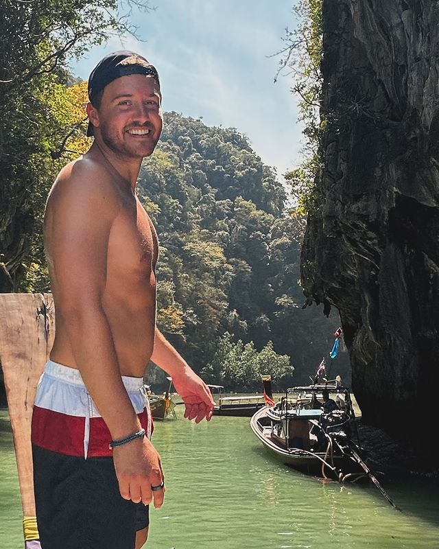 A shirtless man wearing red, white and blue swim trunks and a backward black baseball cap.