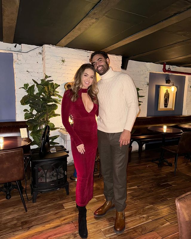 A woman in a low-cut red dress and a man in a white sweater pose together