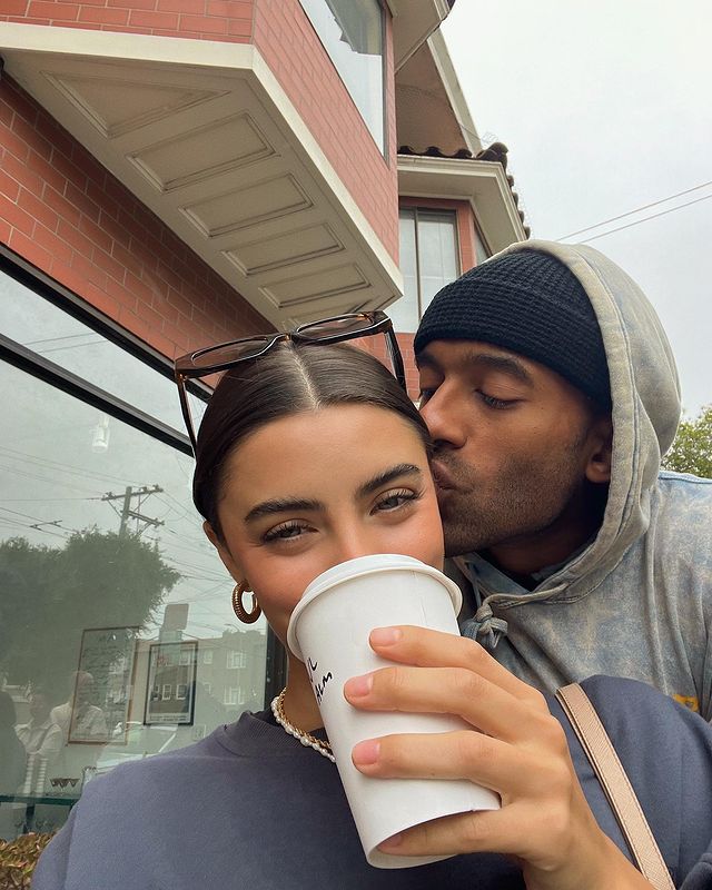 A photo of a woman holding a coffee cup and her boyfriend kissing her forehead.