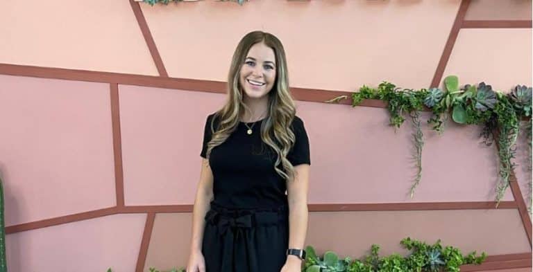 Jana Duggar smiling and posing for a photo in front of a pink wall